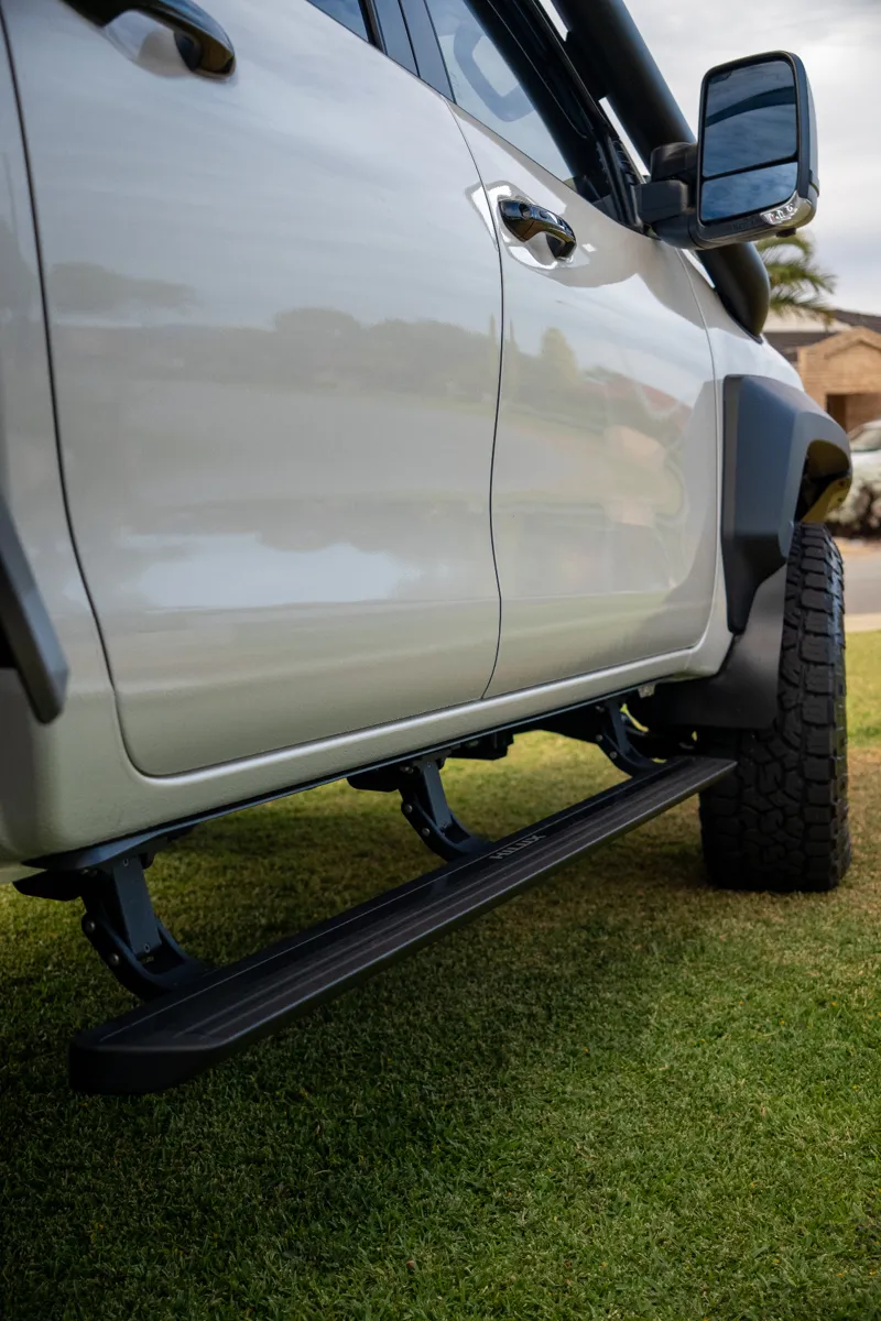 Deployed electric side step beneath a white 4x4
