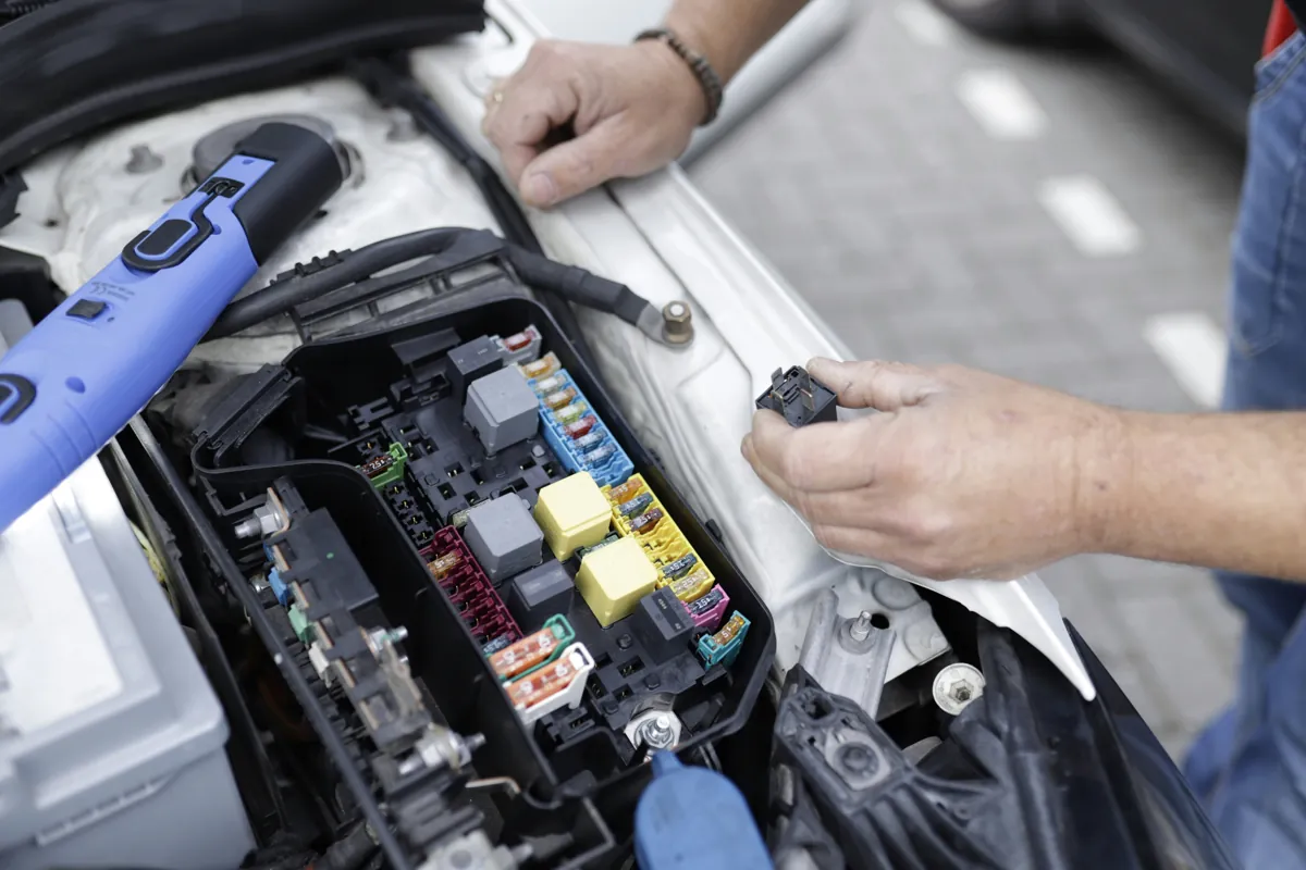 Hands working beside a vehicle fuse box and electrical wiring